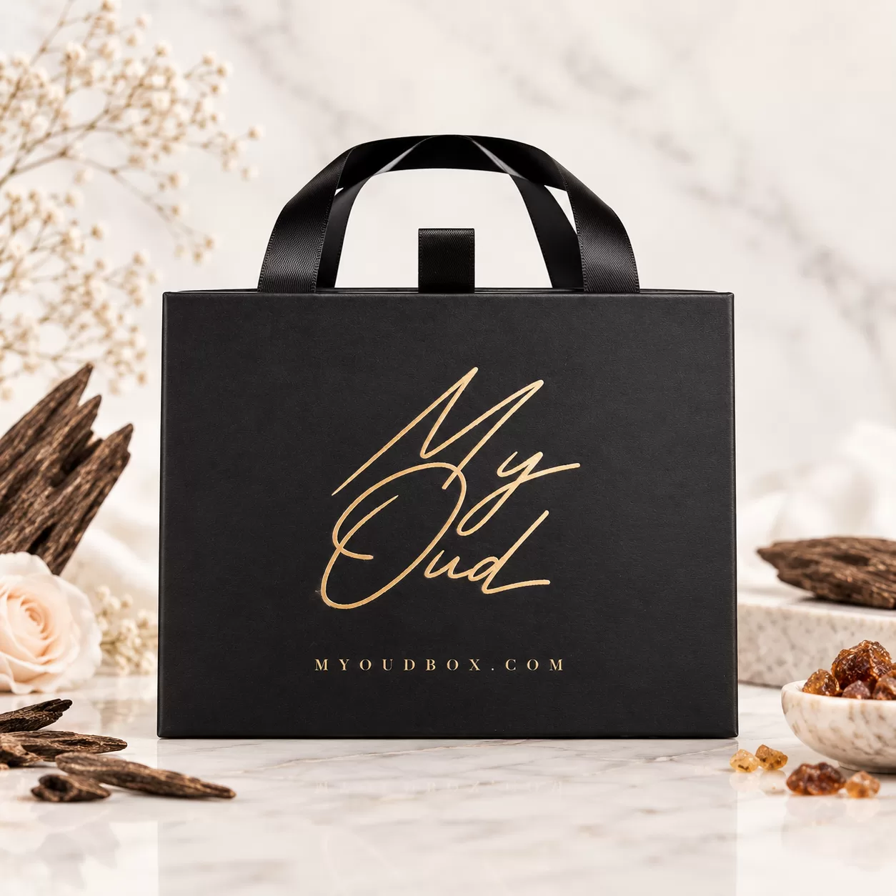Closed black My Oud gift box with ribbon handles and a gold logo.